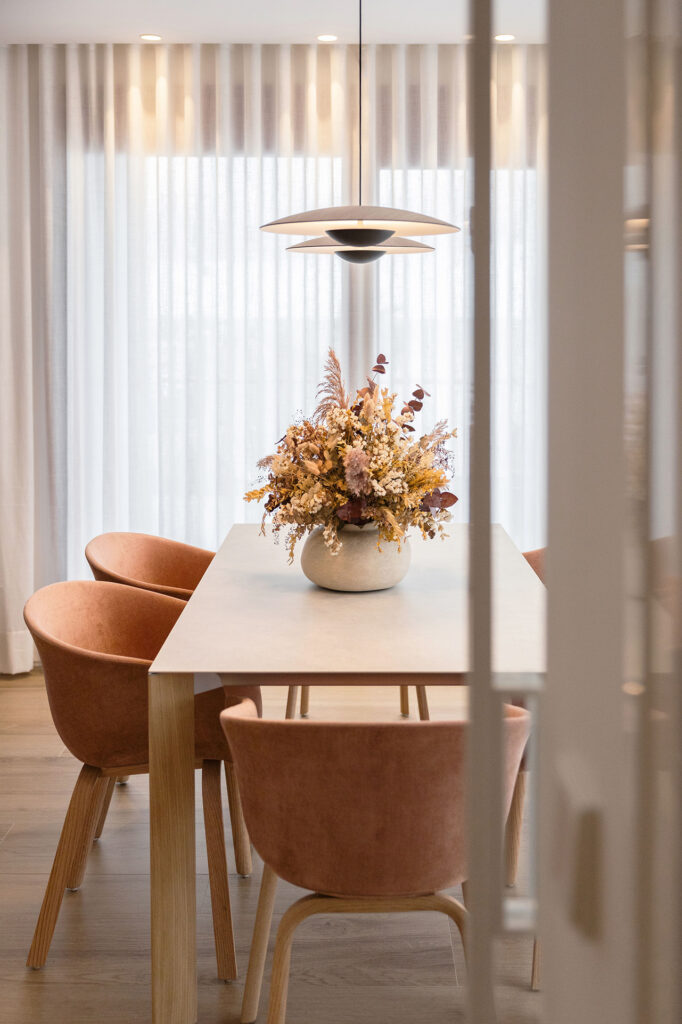 mesa de comedor con sillas alrededor en color rosa empolvado y lamparas de marset